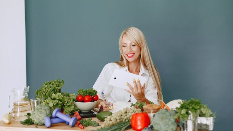 Woman using a tablet surrounded by fresh vegetables at a table, showcasing healthy lifestyle and technology.