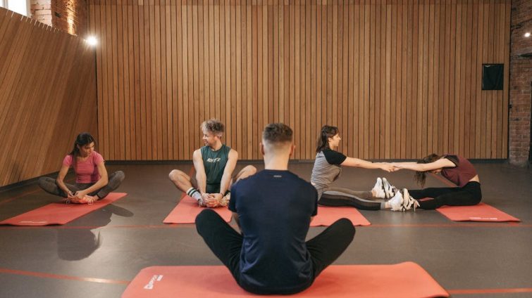 A group of adults practicing yoga and stretching on mats in a wooden panelled room.